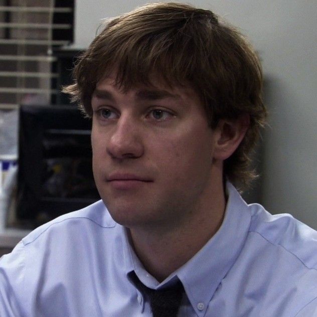 a young man wearing a white shirt and black tie sitting in an office cubicle