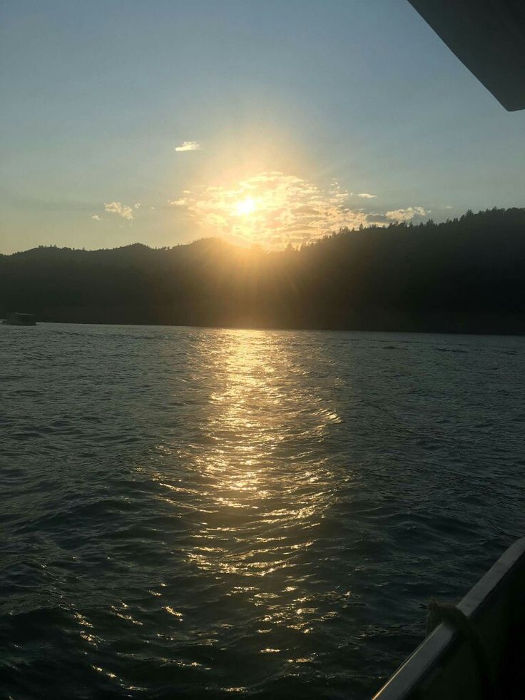 the sun is setting over water with mountains in the background