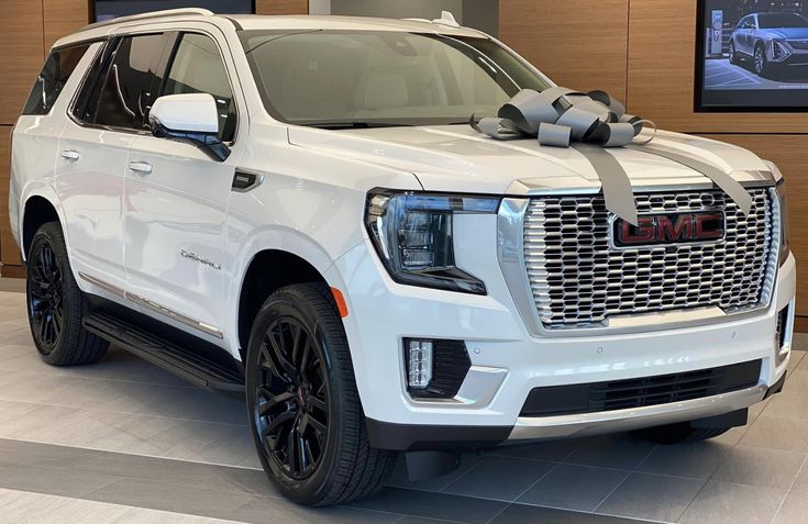 a white truck with a large bow on the hood and front bumper is parked in a showroom