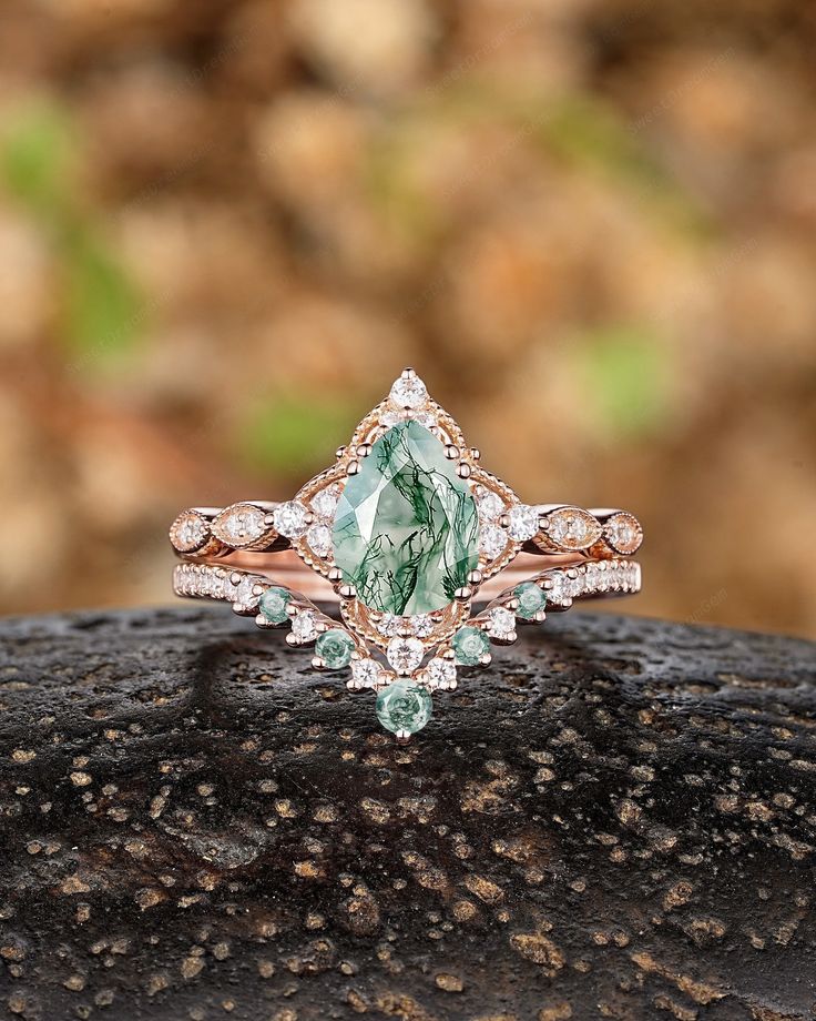 an engagement ring with a pear shaped green stone surrounded by small white diamonds on top of a rock