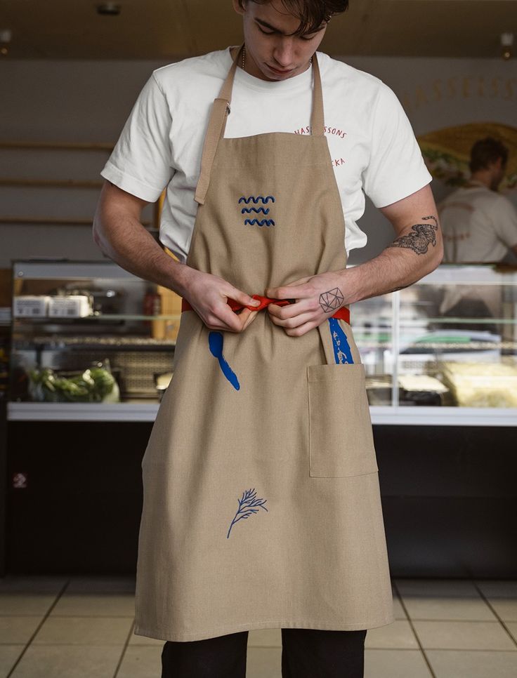 a man in an apron is looking down at his red scissors as he prepares to cut something