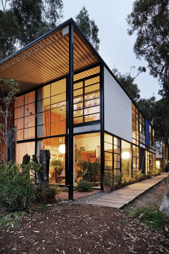 the house is surrounded by trees and plants, with glass walls on each side that allow natural light into the room