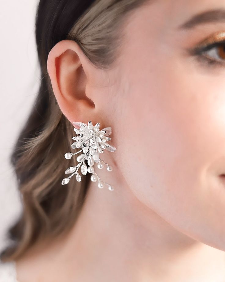 Perfect for adding a whimsical touch to any special occasion look, our Neve Floral Earrings bring a fresh take on timeless glamour. You'll have everyone commenting on these floral inspired statement earrings. Details: Hand wired with mix of light ivory pearls, rhinestones and tulle petals. Made with top grade rhinestones for ultimate sparkle. Specifications: 2" in length x 1.25" wide. Extremely lightweight and easily worn all day and evening. Tarnish Resistant: Earrings are tarnish resistant for Elegant Clip-on Flower Earrings For Party, White Clip-on Bridal Earrings For Party, Delicate Pearl Earrings For Party, Delicate Pearl White Bridal Earrings For Party, Pearl White Flower Earrings With Pearl Drop For Party, Pearl White Flower Pearl Drop Earrings For Party, Party Pearl White Flower Earrings With Pearl Drop, White Crystal Clip-on Earrings For Party, Party Pearl Drop Flower Earrings