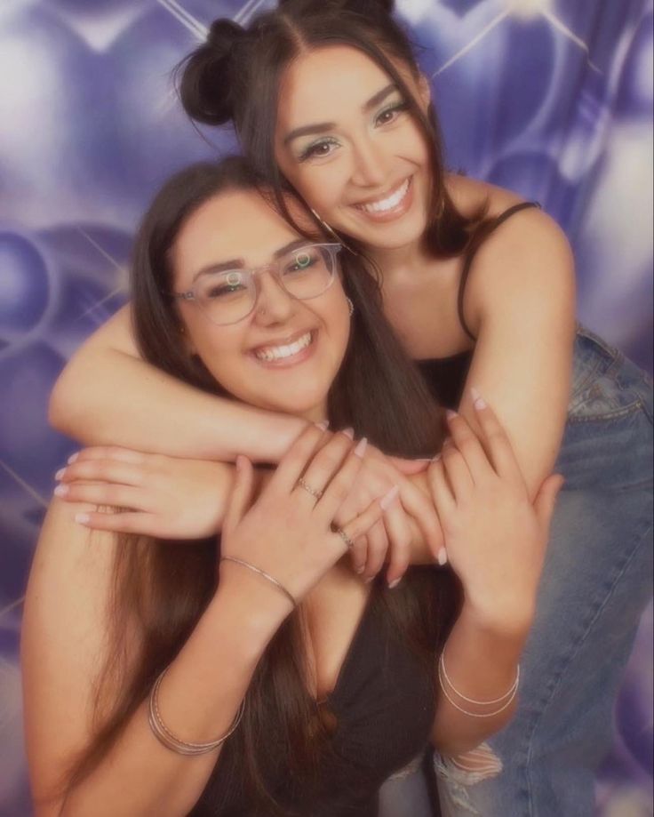 two young women hugging each other in front of a purple background