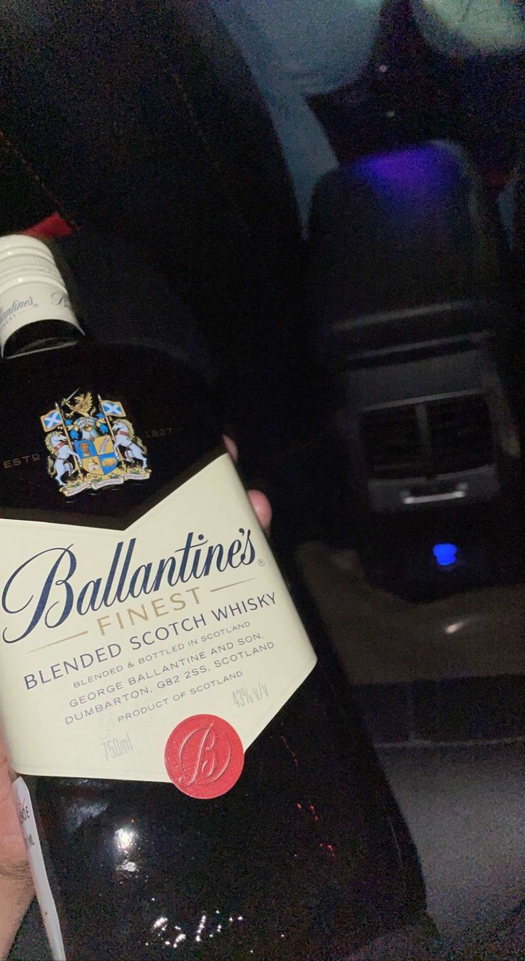 a bottle of ballantines blended scotch whisky in someone's hand on the backseat of a car