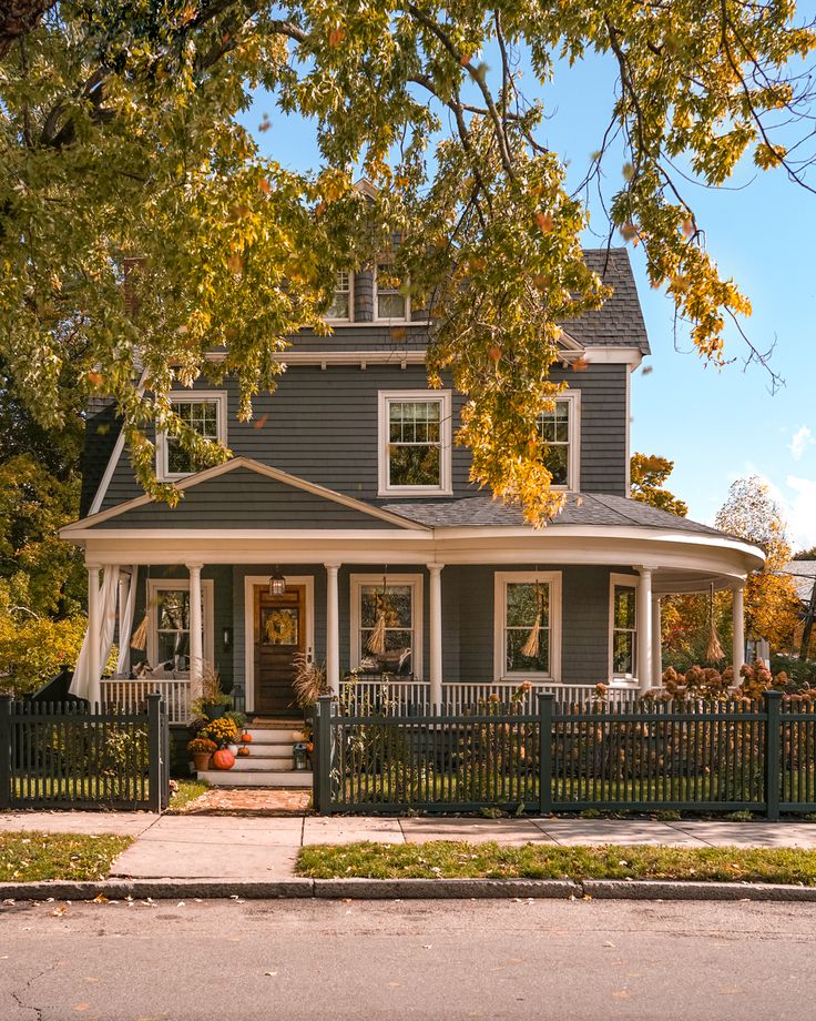 a gray house with white trim on the front porch and fenced in yard area