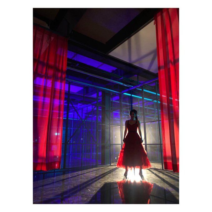 a woman in a red dress standing in front of some bright colored lights and curtains