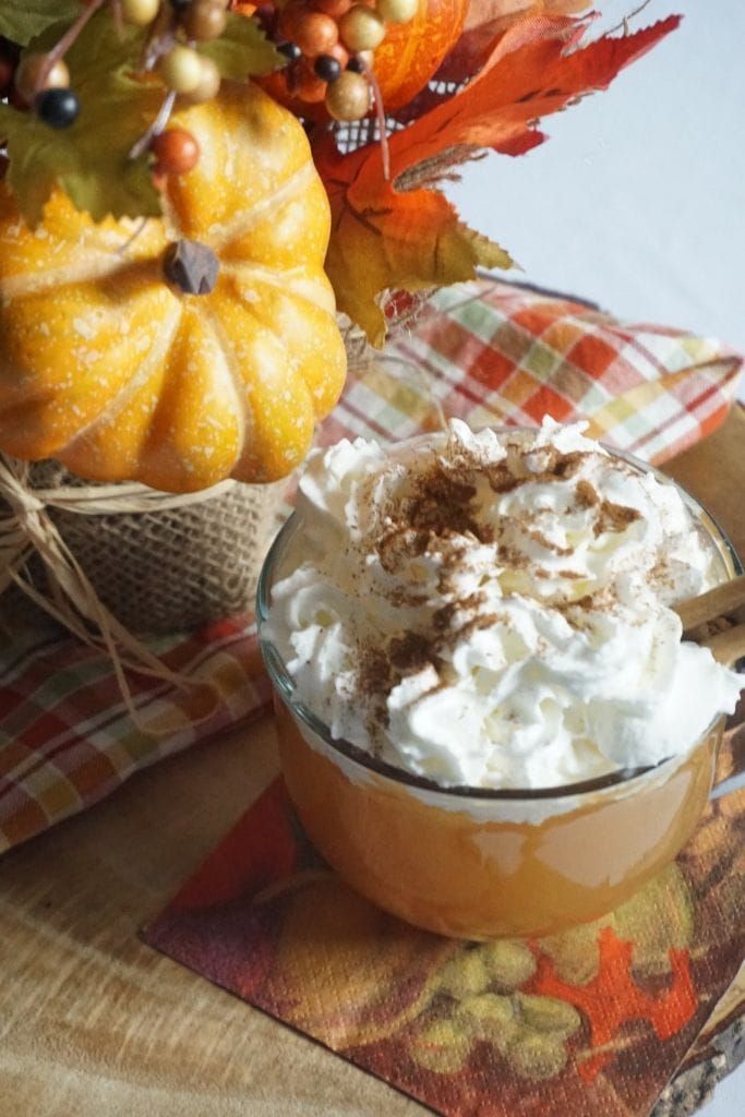 a cup filled with whipped cream sitting on top of a table next to fall leaves