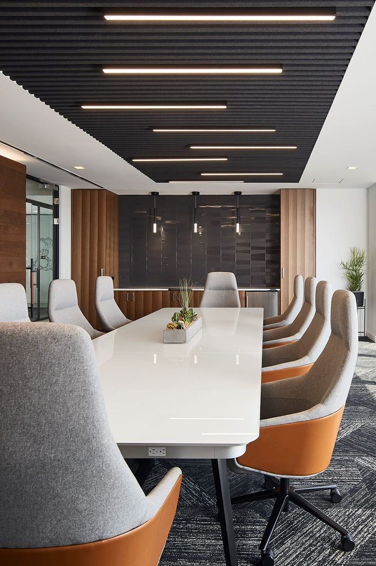 an empty conference room with white tables and orange chairs in front of a black wall