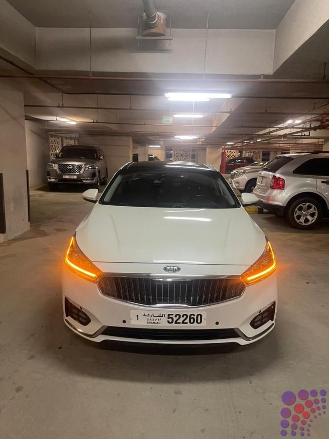 a white car is parked in an underground parking garage with other cars and one has its lights on