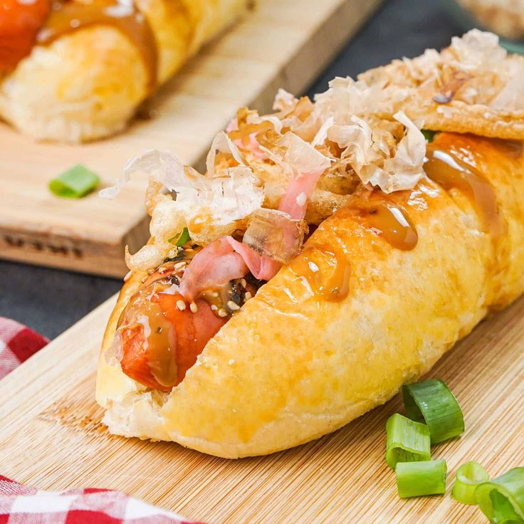 a hot dog with toppings sitting on top of a cutting board next to other food items