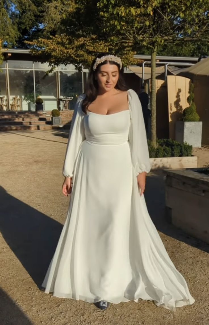 a woman in a white dress standing on the ground wearing a tiara and long sleeves