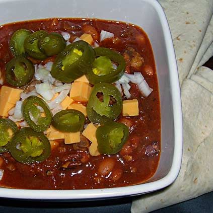 a white bowl filled with chili, cheese and jalapenos on top of a table