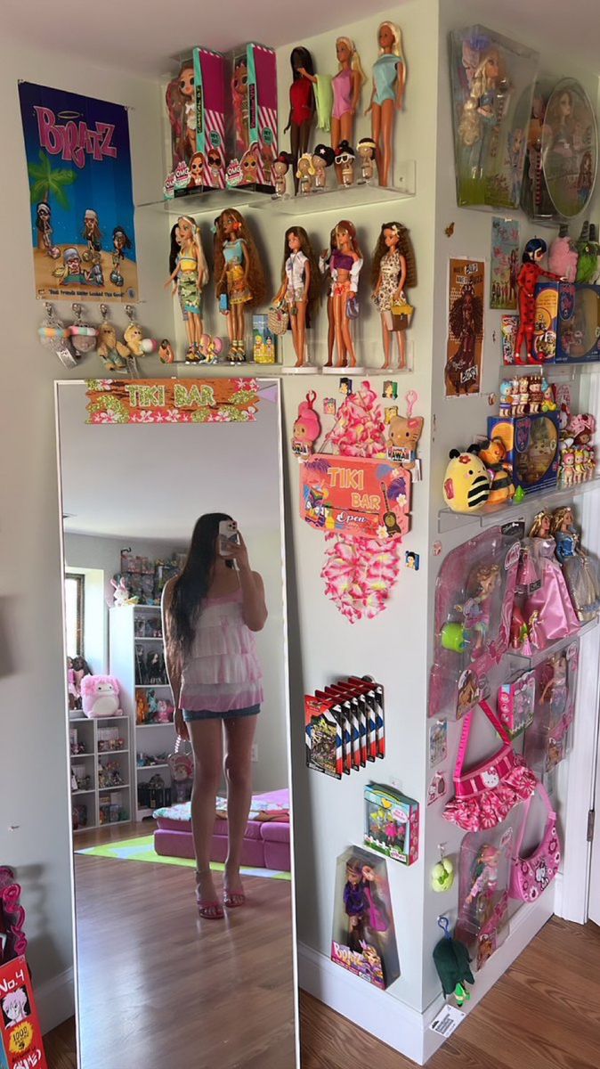 a woman taking a selfie in front of a refrigerator with barbie dolls on it