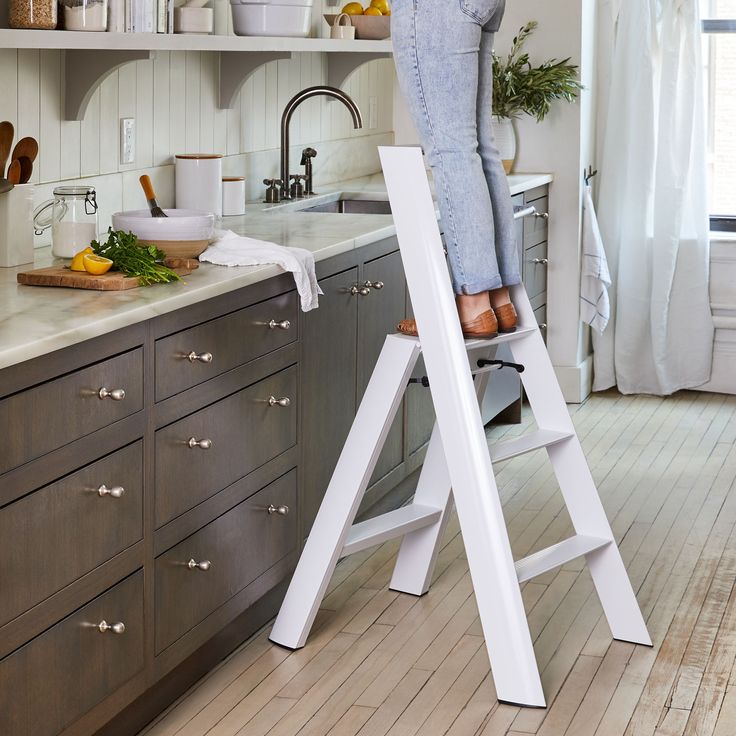 a woman is standing on a ladder in the kitchen and she has her feet up