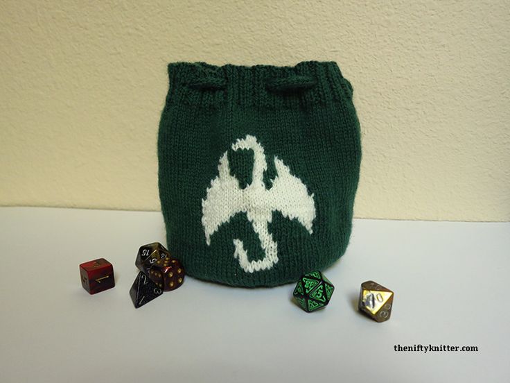 a green knitted bag with white letters and dice on the side next to it