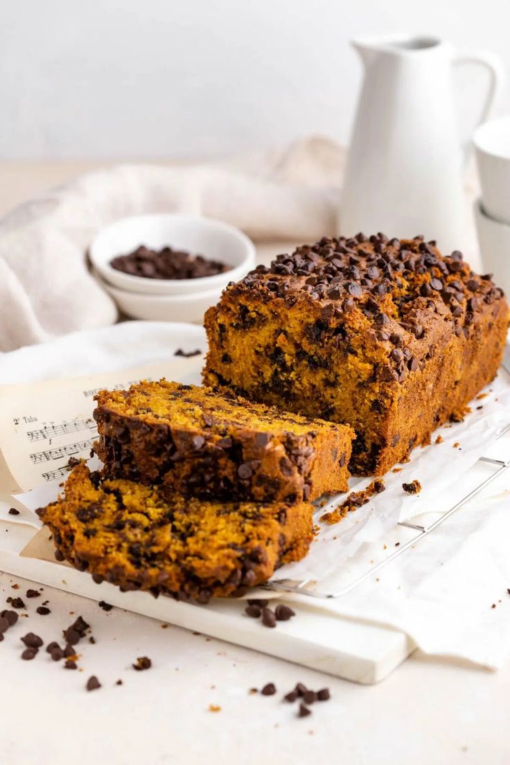 a loaf of chocolate chip pumpkin bread on a cutting board next to two mugs