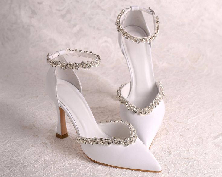 a pair of white high heeled shoes with crystal embellishments