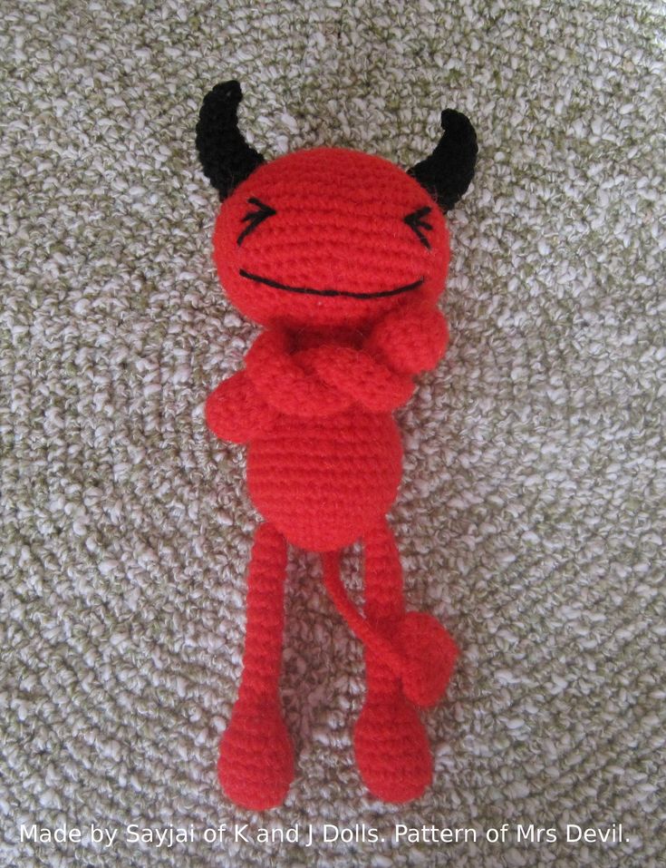 a crocheted red stuffed animal laying on top of a white carpet with black horns