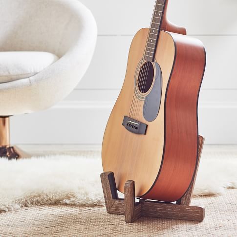 an acoustic guitar on a stand in front of a white chair with a sheepskin rug