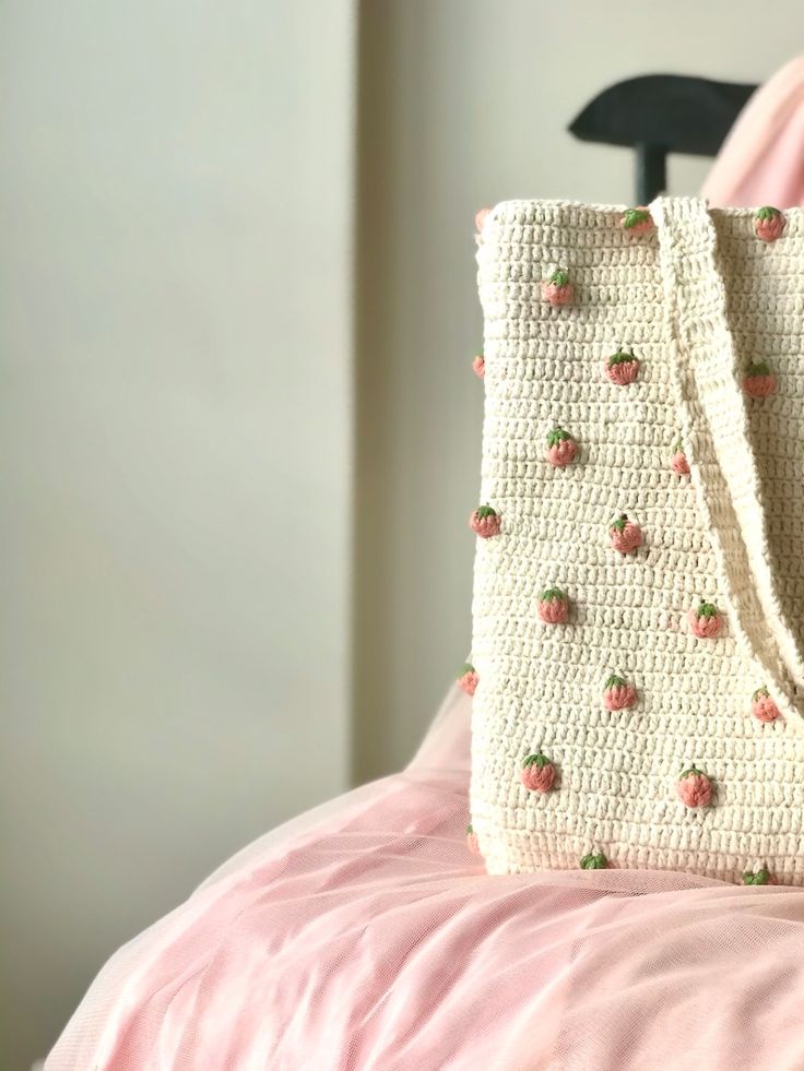 a crocheted strawberries bag sitting on top of a pink comforter next to a black chair