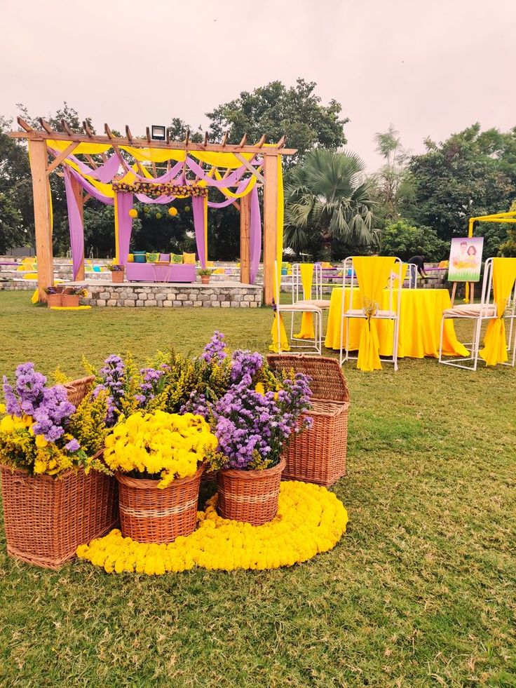 yellow and purple flowers are in baskets on the grass near an outdoor ceremony set up