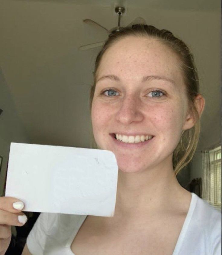 a woman holding up a piece of paper in front of her face and smiling at the camera