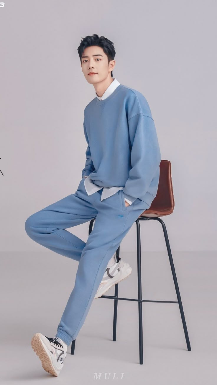 a young man sitting on top of a chair wearing blue sweatpants and white sneakers