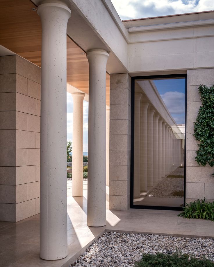 an outside view of a building with columns and plants growing on the side of it