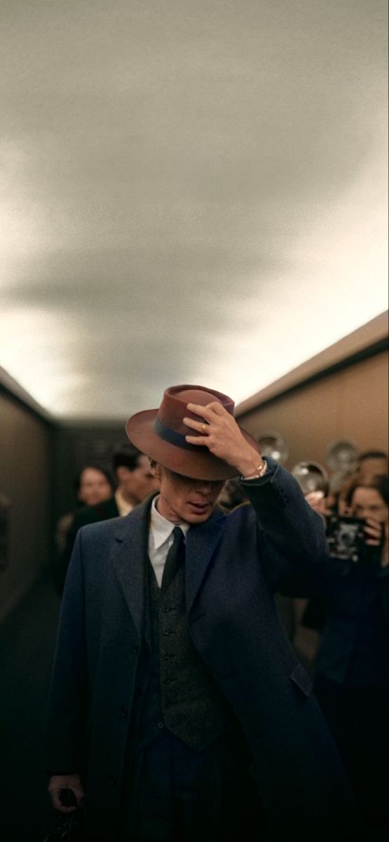 a man in a suit and hat walking down a hallway with other people behind him