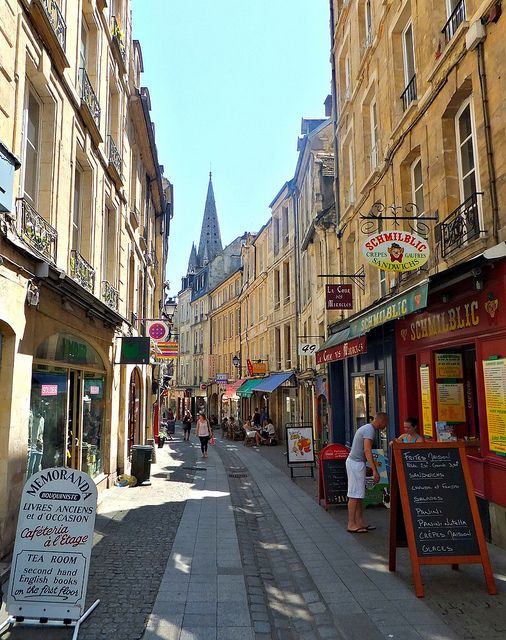 people are walking down the street in an old european city with shops and restaurants on both sides