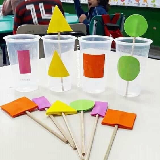 plastic cups with different colored shapes and sticks sticking out of them, sitting on a table