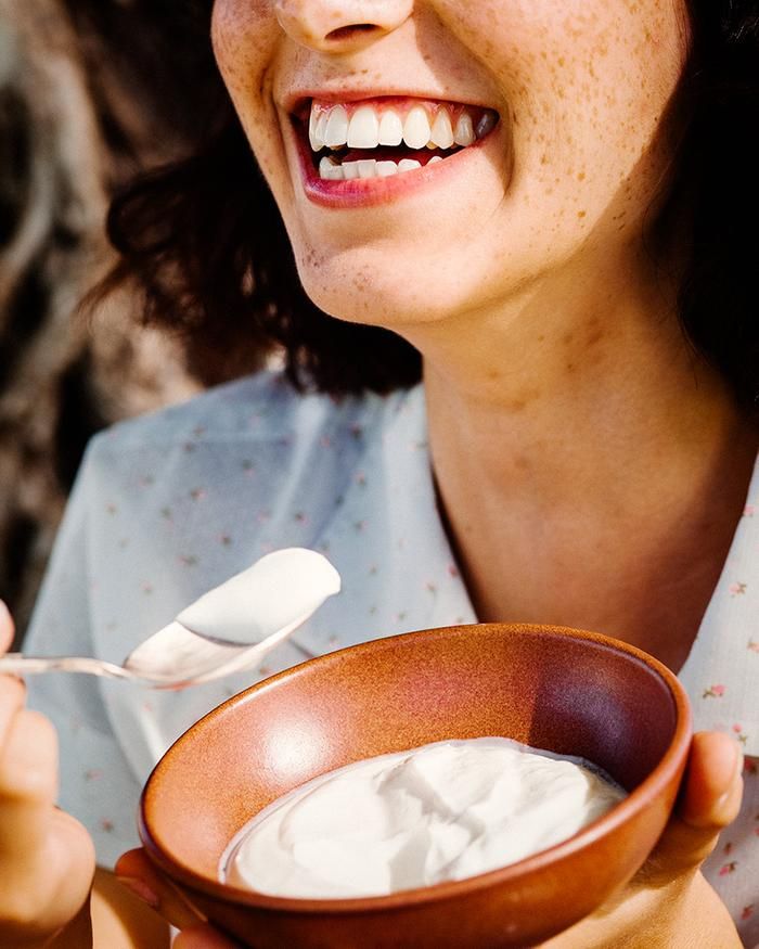 a woman smiles while holding a bowl of yogurt and a spoon in her hand