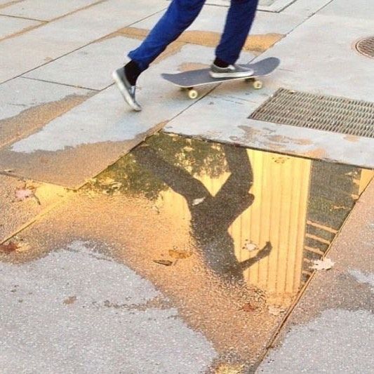 a man riding a skateboard on top of a puddle in the street next to a tree