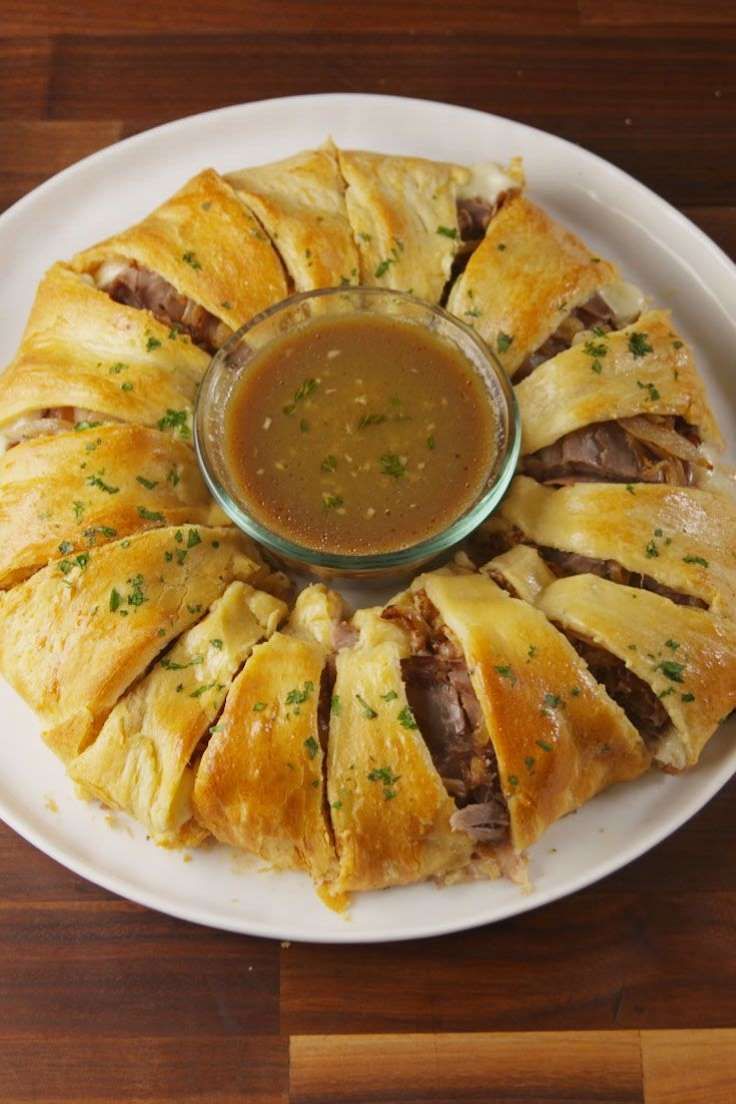 a white plate topped with pastry covered in meat and sauce next to a bowl of dipping sauce