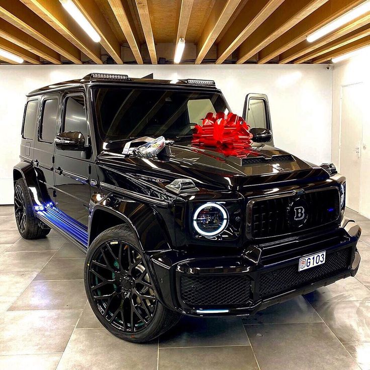 a black mercedes g - class with a red bow on the hood is parked in a garage