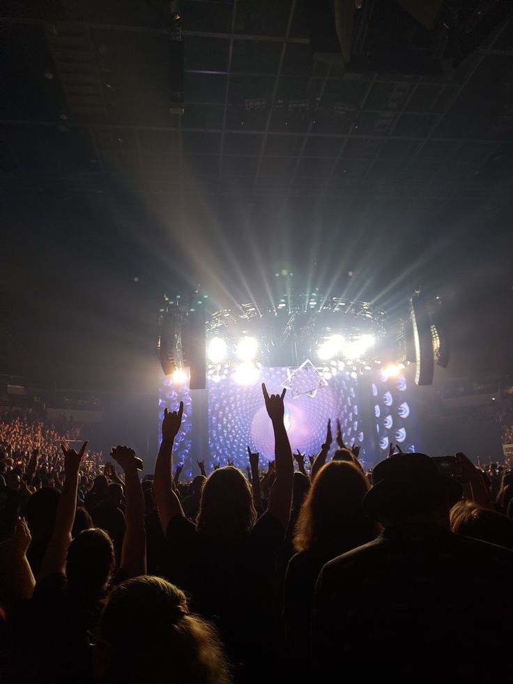 a large crowd at a concert with their hands up in the air and lights on