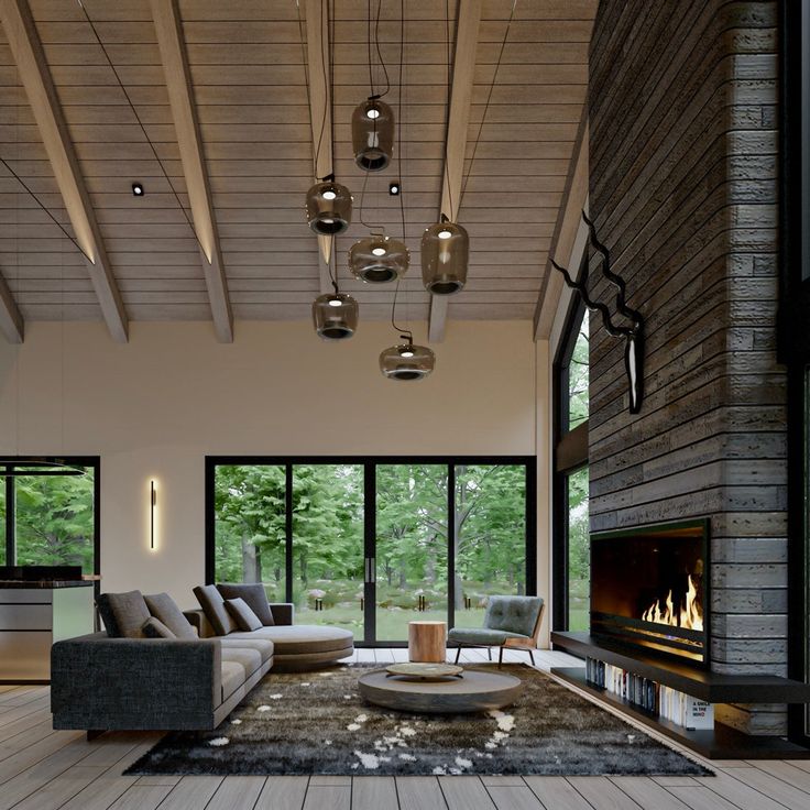 a modern living room with wood floors and large windows overlooking the forest is lit by pendant lights that hang from the ceiling