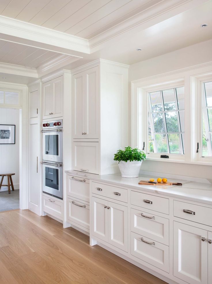 a kitchen with white cabinets and an oven in the center is seen from across the room