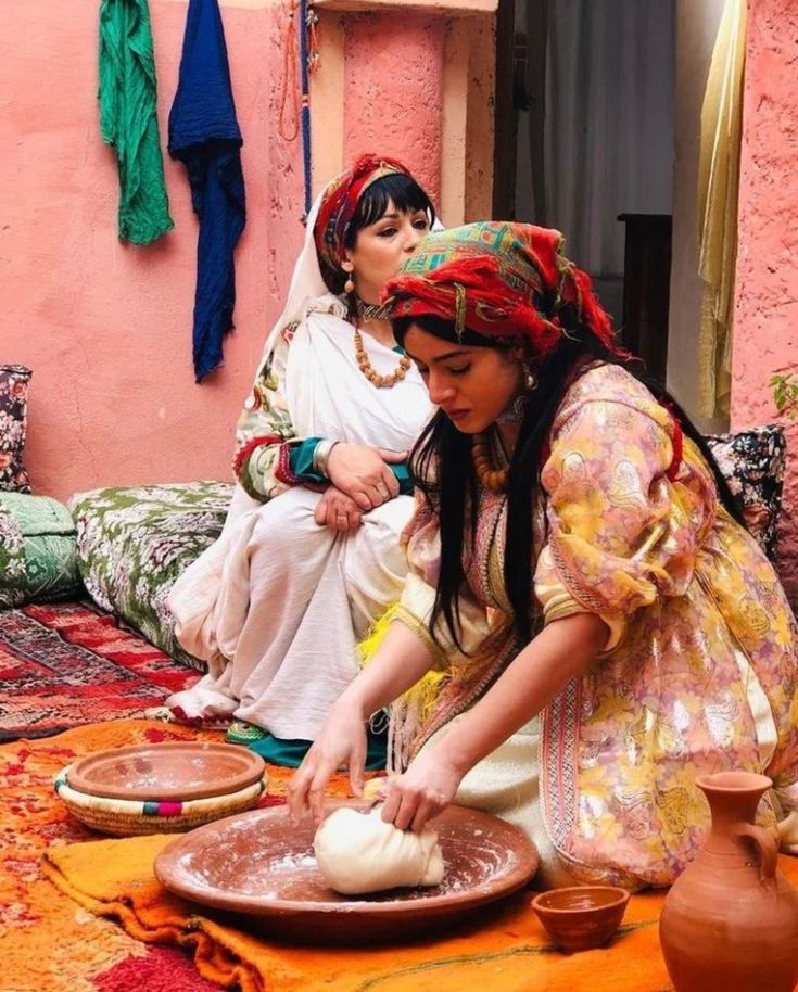 two women are making bread on the floor in front of a pink wall and rug