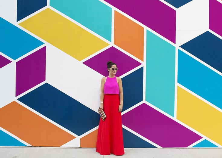 a woman in a long red dress standing next to a wall with colorful geometric designs