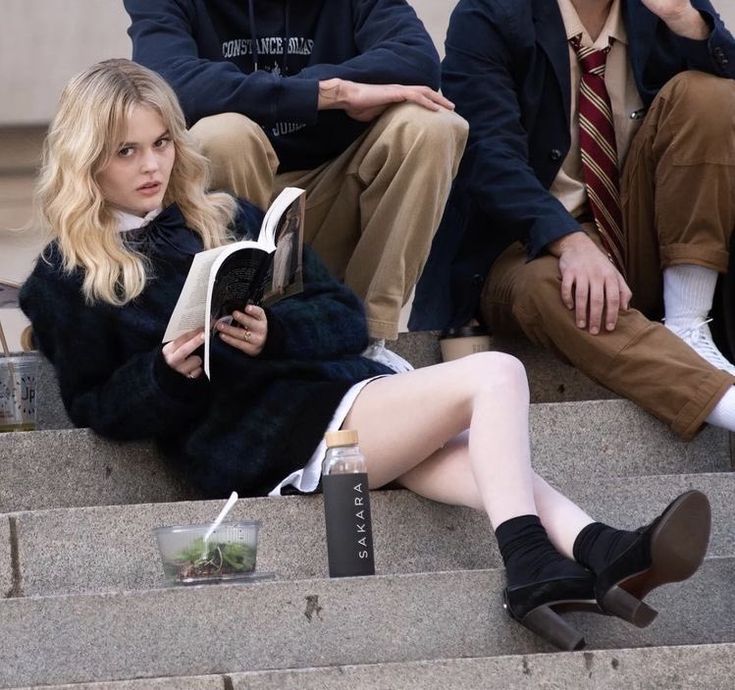 three people sitting on the steps with one reading a book and another looking at her cell phone