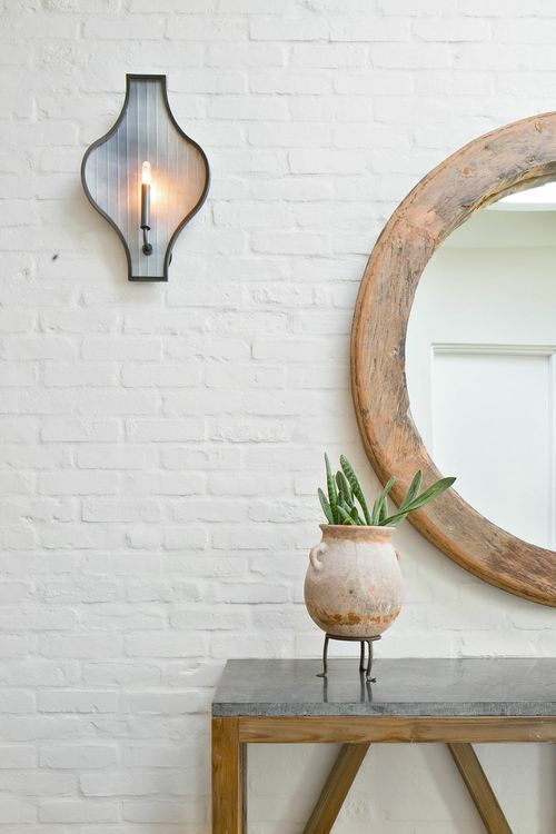 a white brick wall with a mirror and potted plant on a bench in front of it