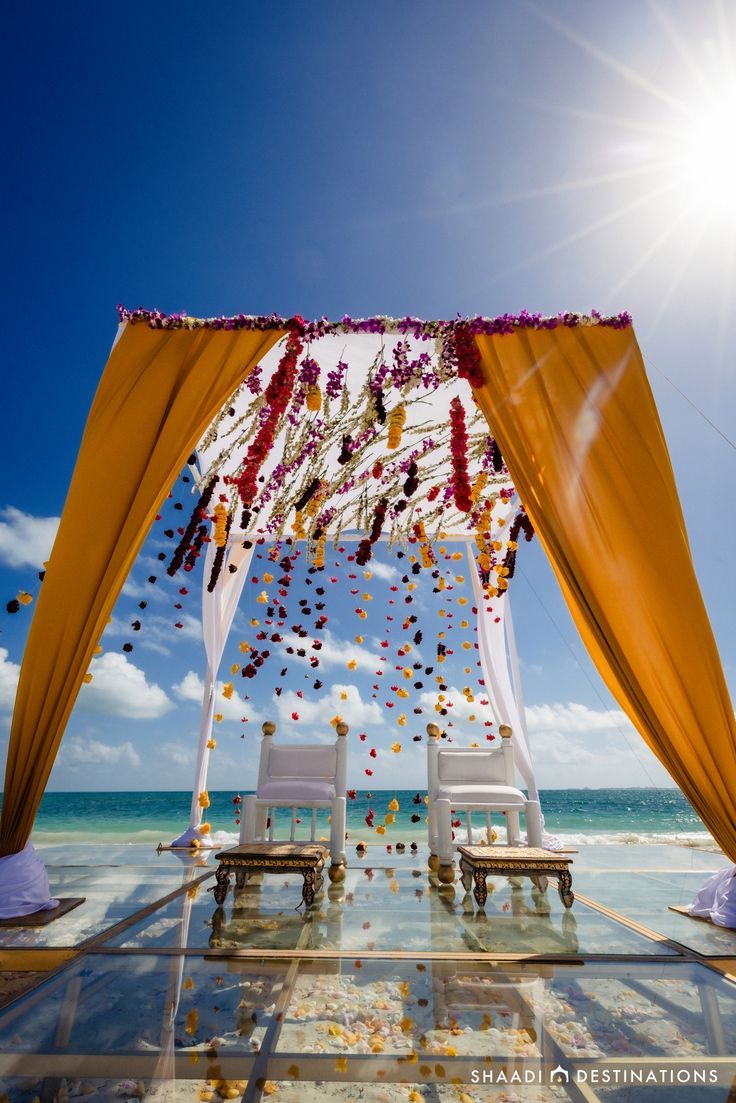 an outdoor ceremony set up with white chairs and yellow draping on the beach