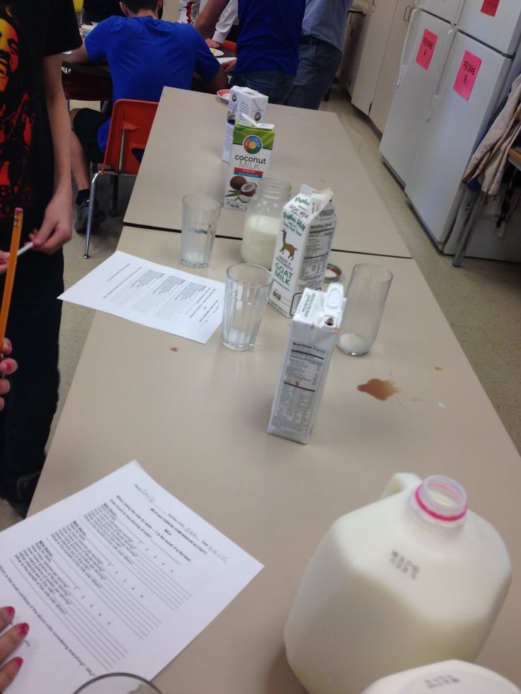 several people are gathered around a table with milk and other items on it, as one person holds a pencil