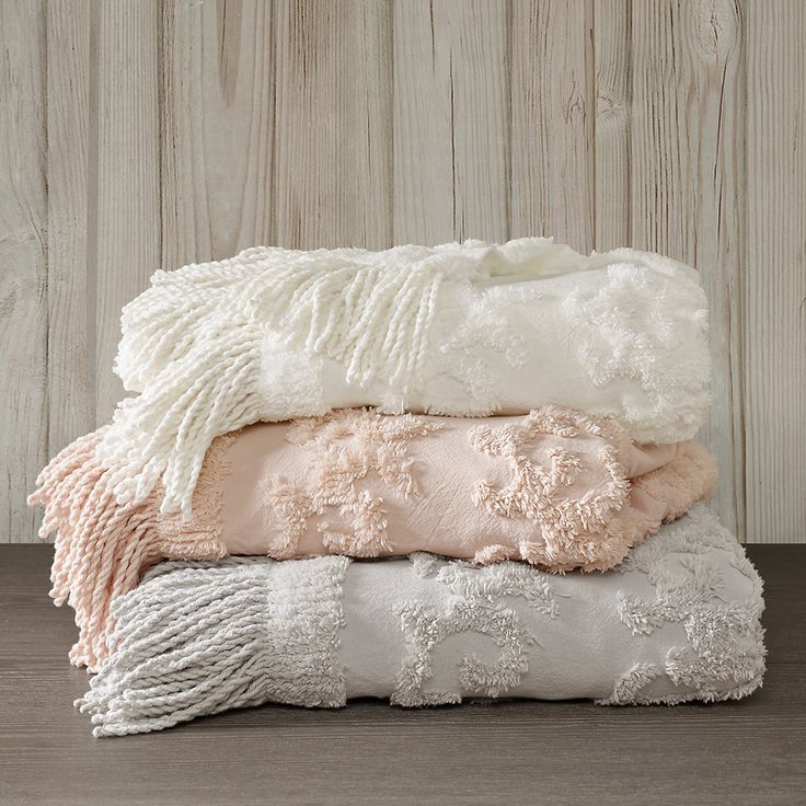 three blankets stacked on top of each other in front of a wooden wall and floor