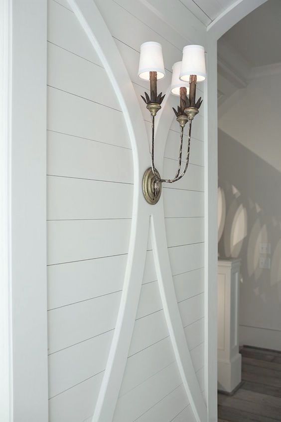 two lights are attached to the side of a white wall with wood flooring in front of it