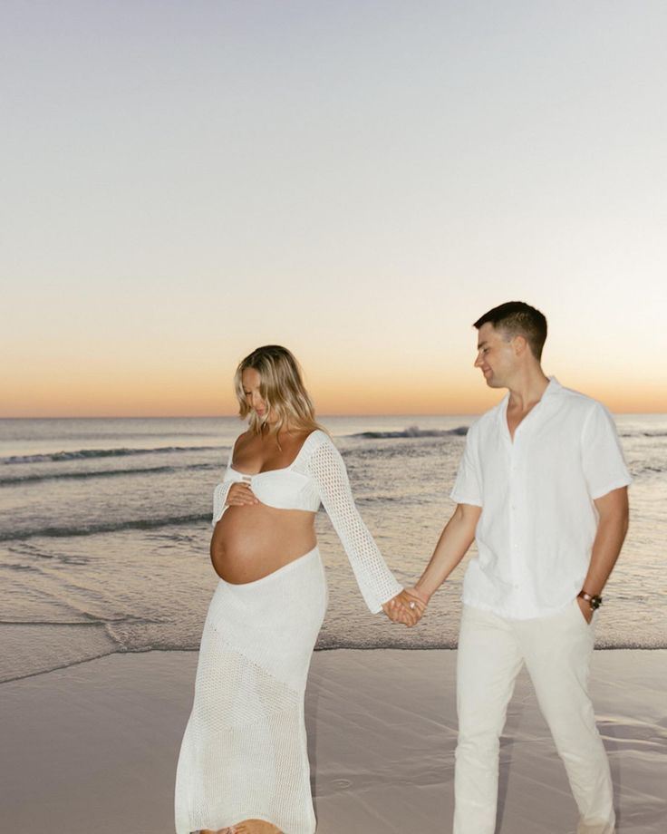 a pregnant couple holding hands on the beach