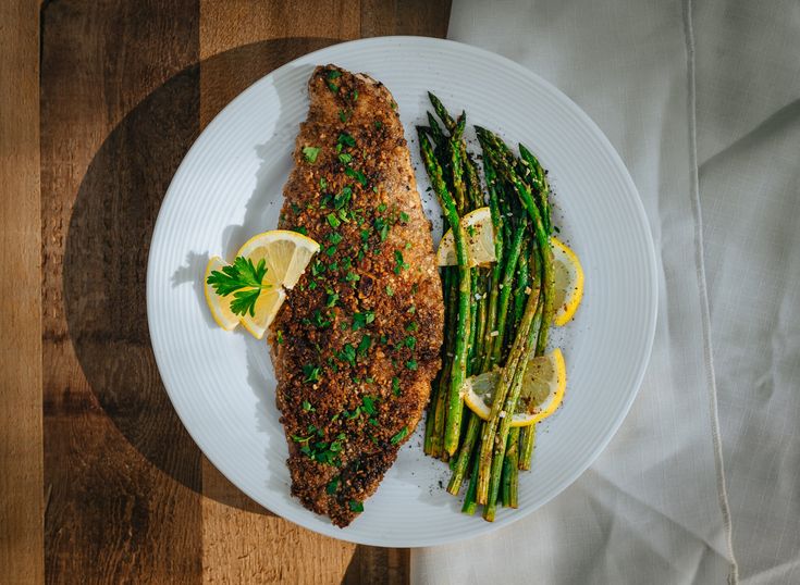 a white plate topped with fish and asparagus on top of a wooden table