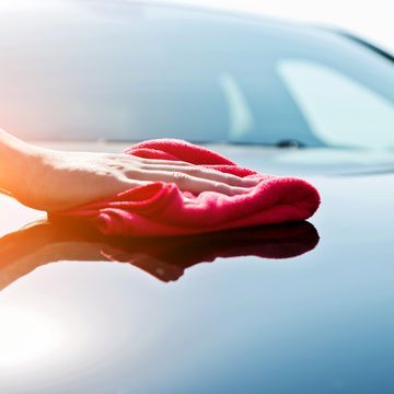 a person's hand with a microfiber on the hood of a car